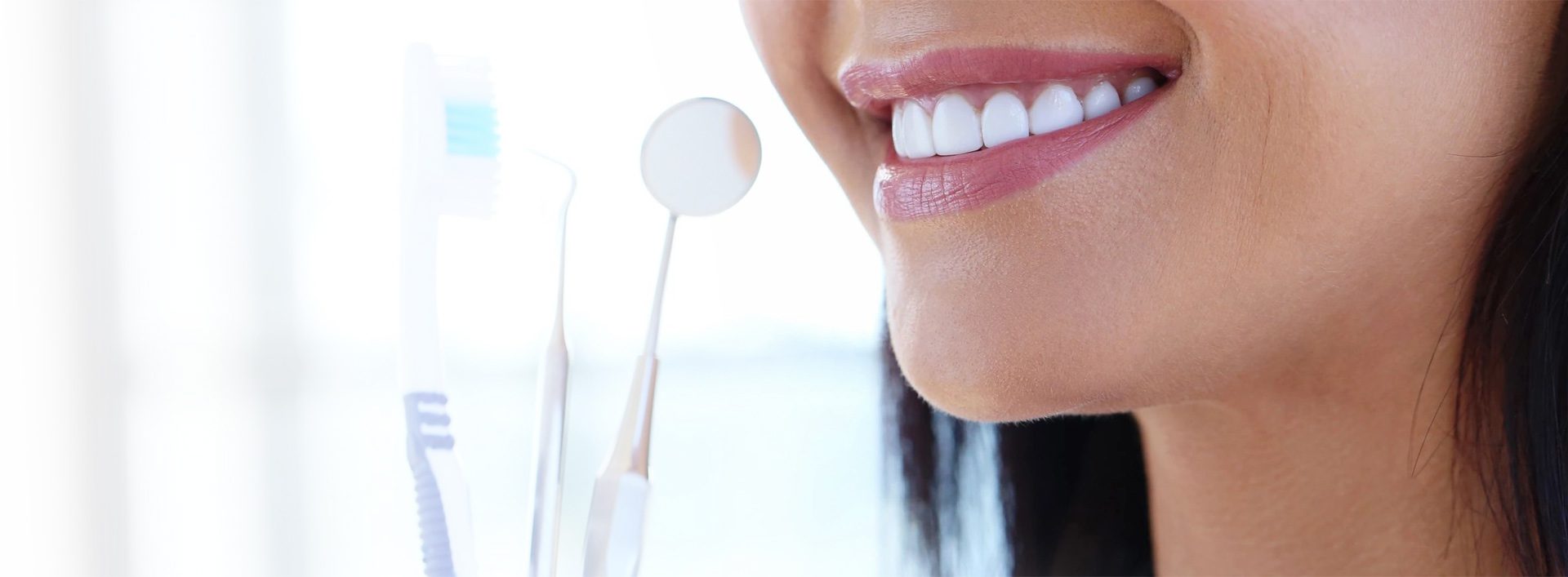 A woman with white teeth and two tooth brushes.