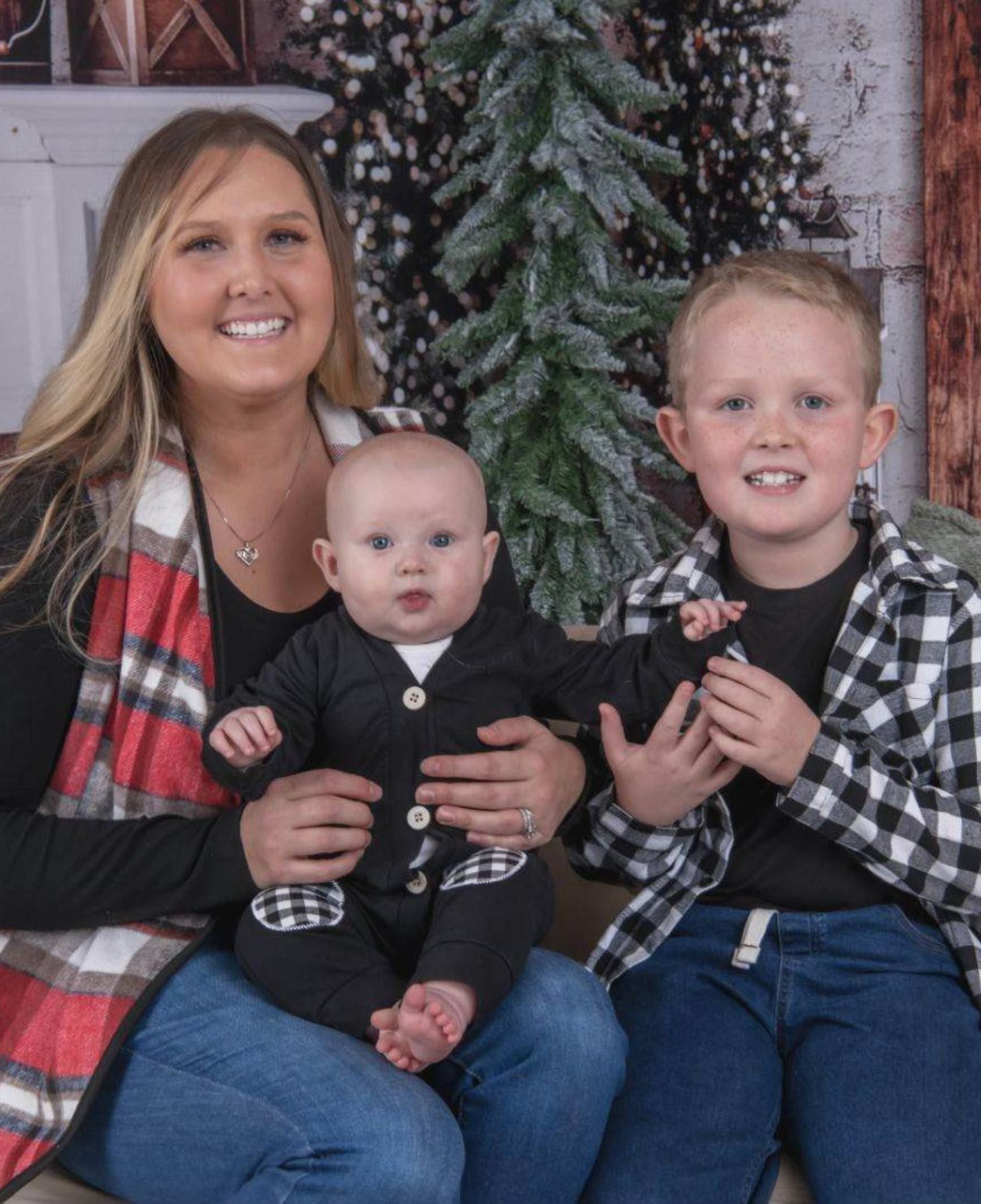 A woman and two boys sitting in front of a christmas tree.